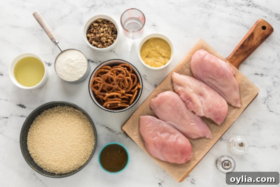 A flat lay photograph showing all the ingredients neatly arranged for the pretzel chicken recipe, including chicken breasts, pretzels, walnuts, panko breadcrumbs, honey, mustard, and olive oil.