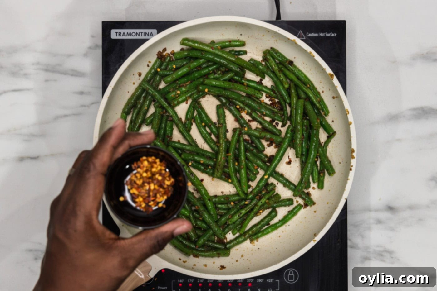 hand holding red pepper flakes over sauteed green beans