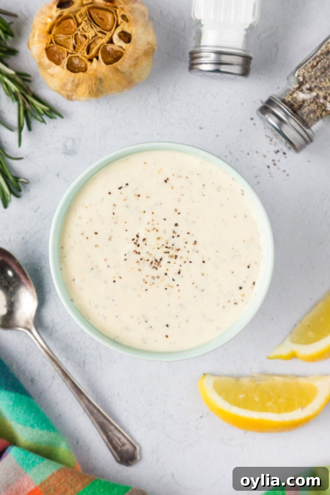 Homemade Garlic Aioli 7 A beautifully composed shot of a bowl of homemade Roasted Garlic Aioli, artfully arranged with fresh lemons, whole roasted garlic cloves, a sprinkle of salt, and black pepper, ready to be served.