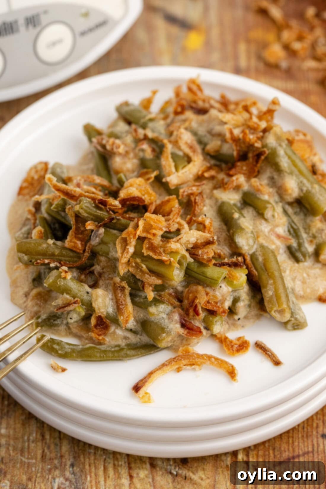 A serving of Crockpot Green Bean Casserole on a white plate, showcasing its creamy texture and crispy onion topping