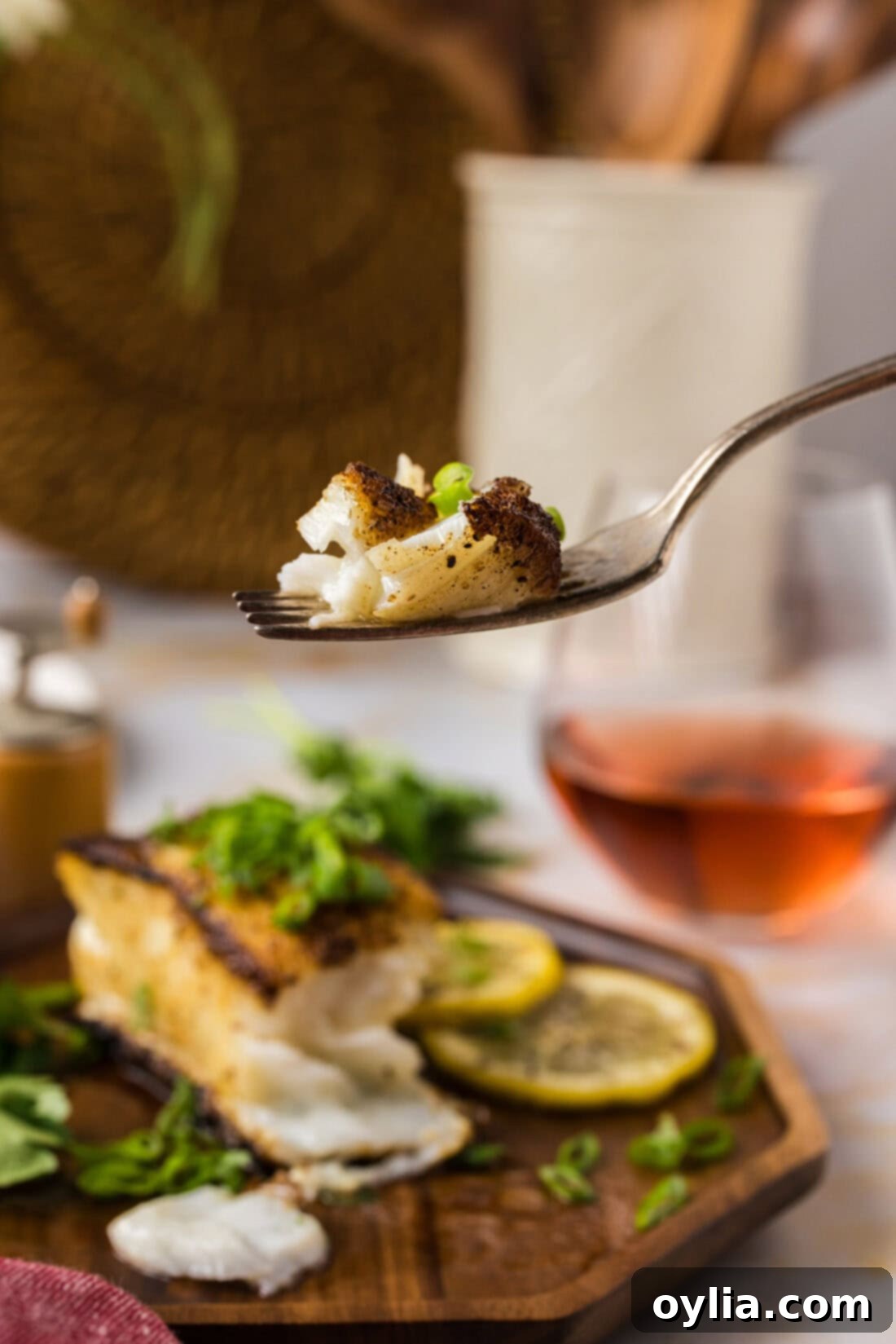Perfectly Pan-Seared Chilean Sea Bass 11 Piece of Pan Seared Chilean Sea Bass on a fork held above a plate of Pan Seared Chilean Sea Bass