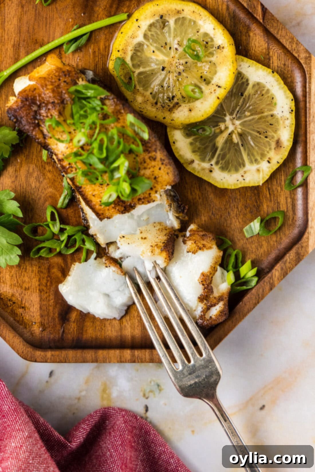 Perfectly Pan-Seared Chilean Sea Bass 3 Overhead photo of a Pan Seared Chilean Sea Bass filet on a plate with a fork and lemons on the side