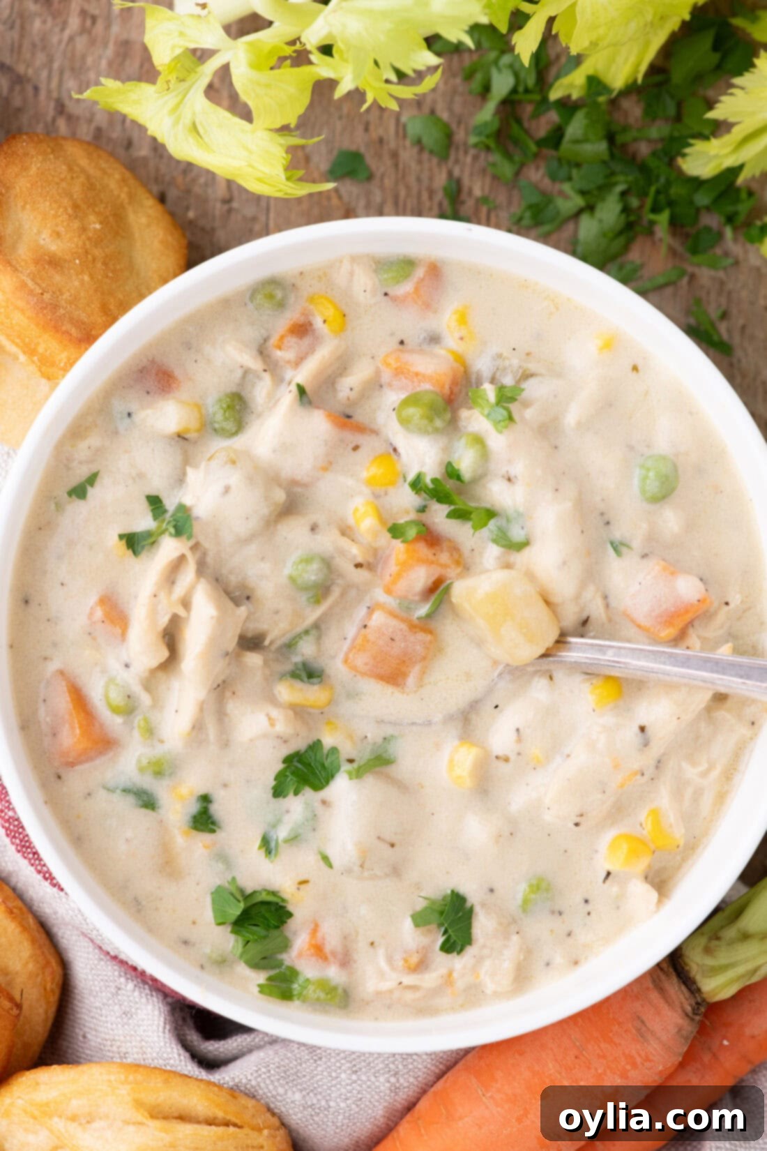 A close-up shot of a single bowl of rich and creamy chicken pot pie soup, garnished with fresh herbs and surrounded by scattered vegetables.