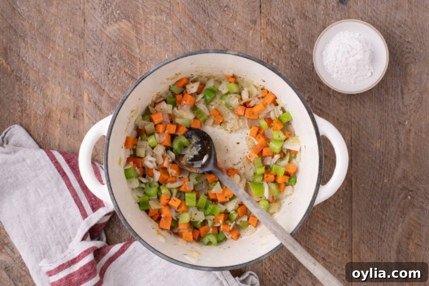 Sautéed vegetables in a Dutch oven, seasoned with garlic, thyme, salt, and pepper, releasing their aromas.