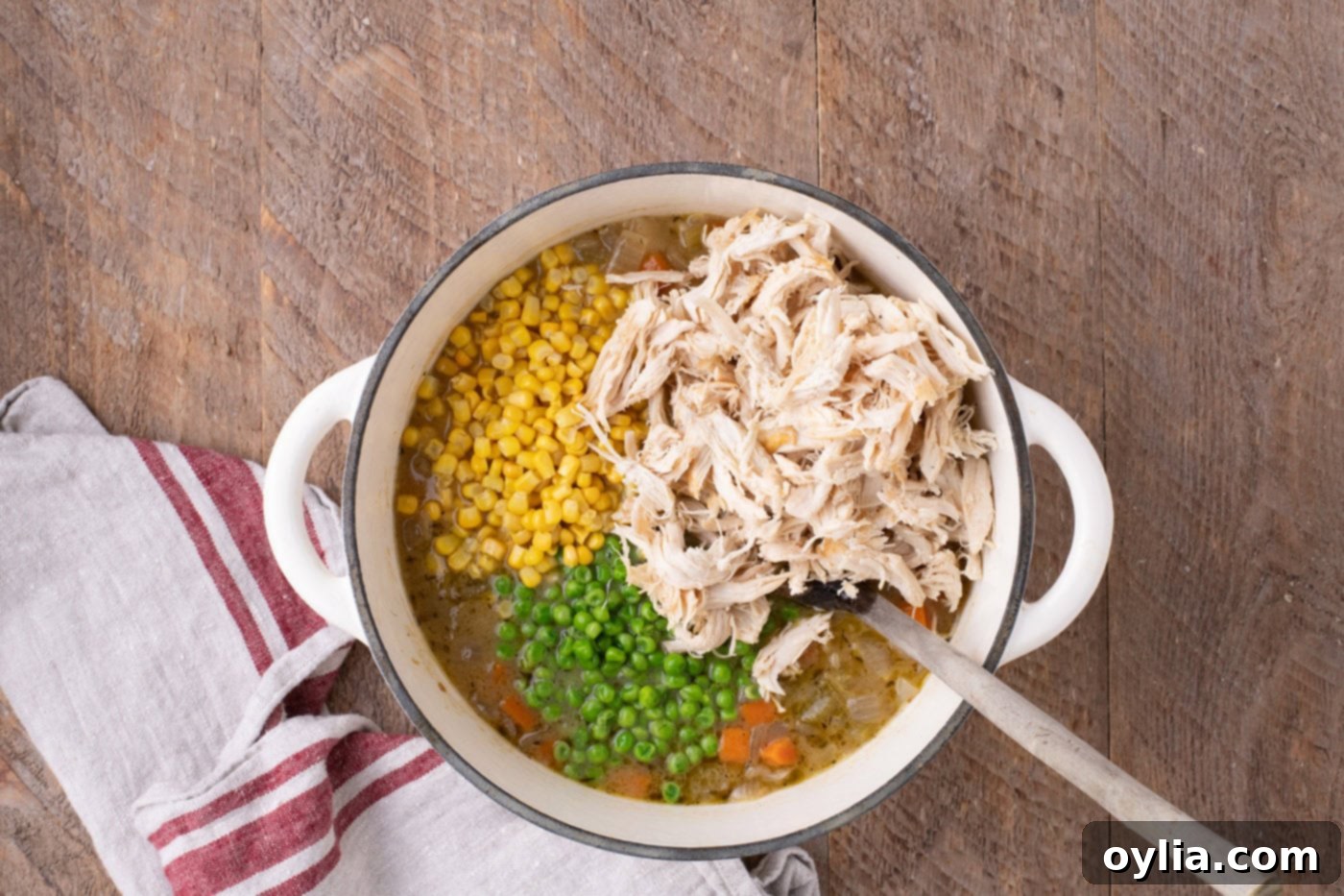 Shredded chicken, frozen peas, and corn being added to the simmering chicken pot pie soup in a Dutch oven.