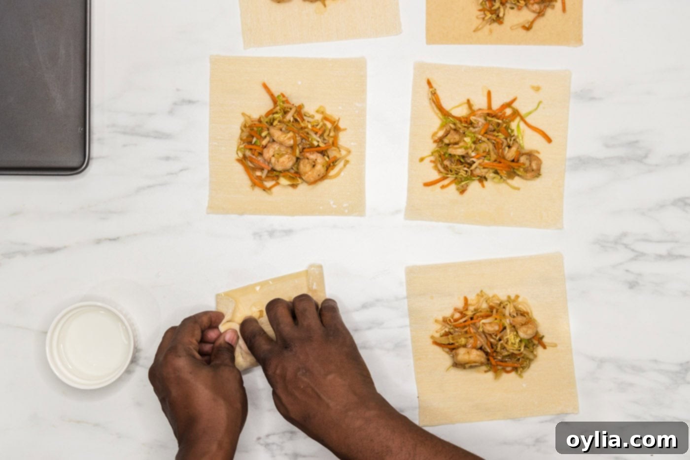 A hand expertly rolling the egg roll to create a tight, sealed cylinder, ready for frying
