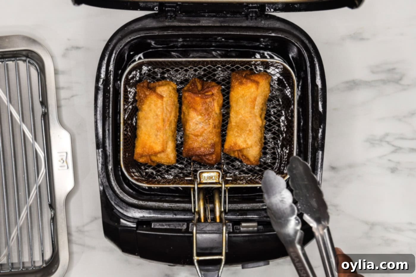 Tongs carefully removing a perfectly deep-fried, golden-brown egg roll from a fryer basket