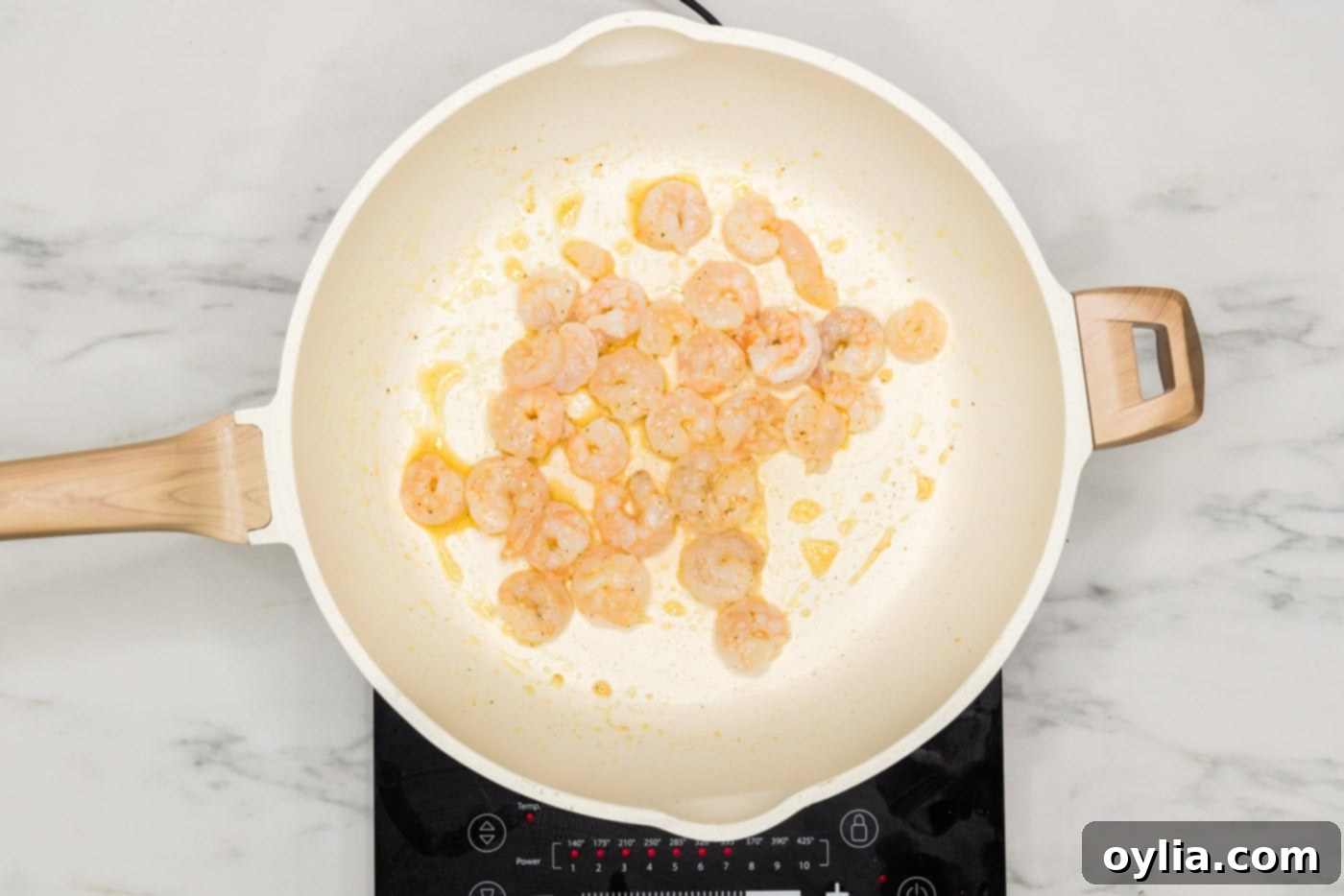 Small raw shrimp cooking in a skillet with seasonings, turning pink