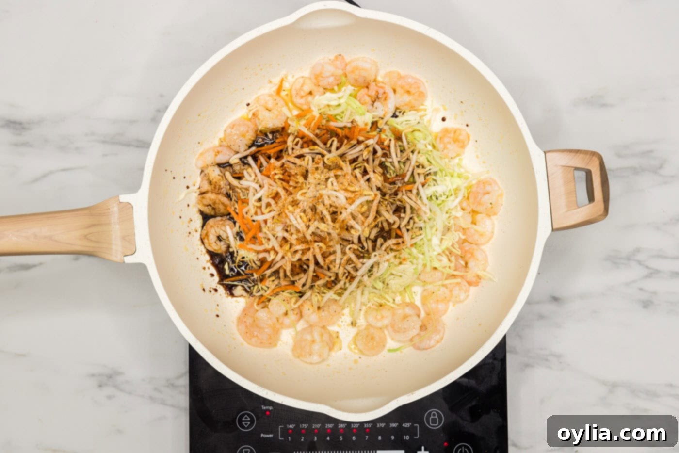 Soy sauce being added to a skillet containing cooked shrimp, bean sprouts, carrots, and cabbage, creating the egg roll filling