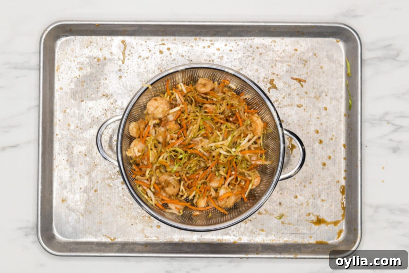 Cooked egg roll filling with shrimp and vegetables draining in a colander, with excess liquid visible