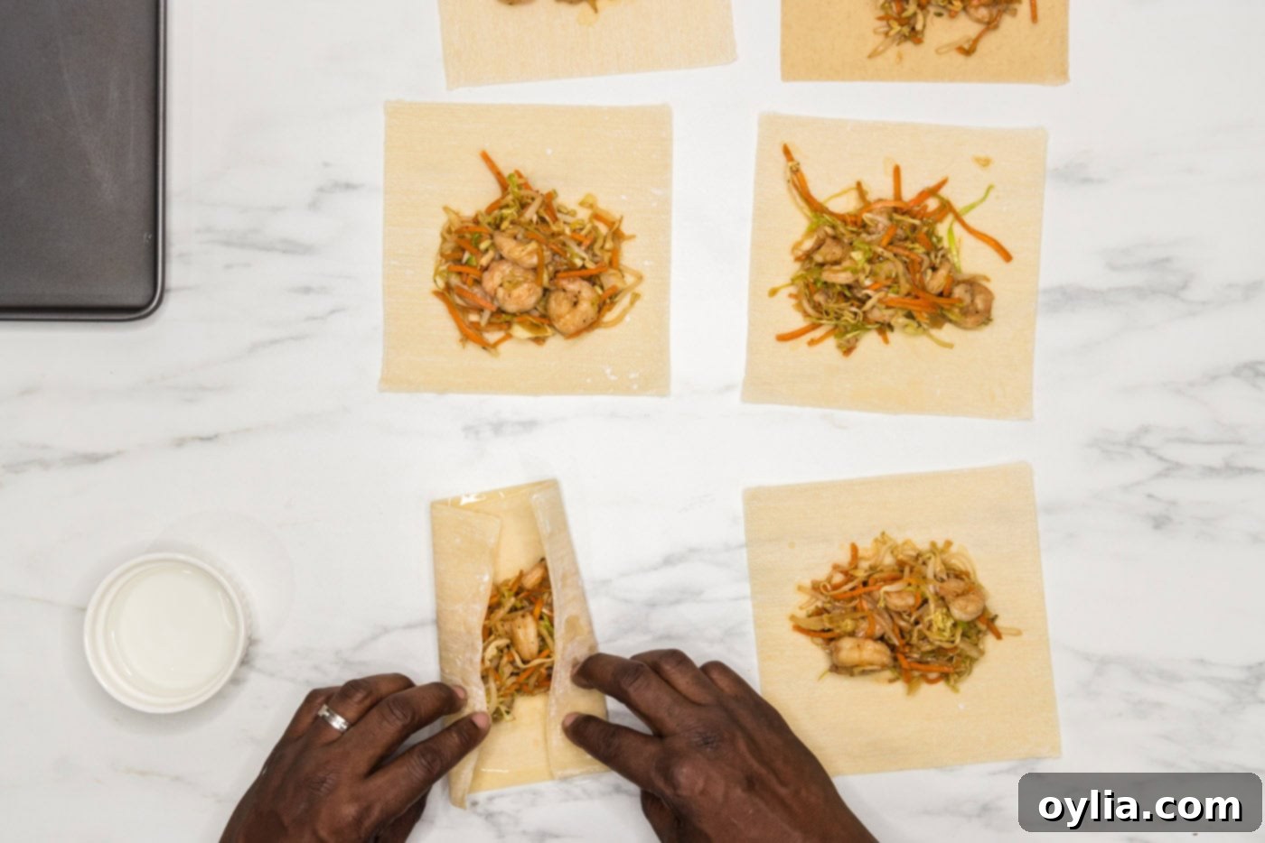 A hand folding the sides of an egg roll wrapper over the filling, demonstrating the initial rolling technique
