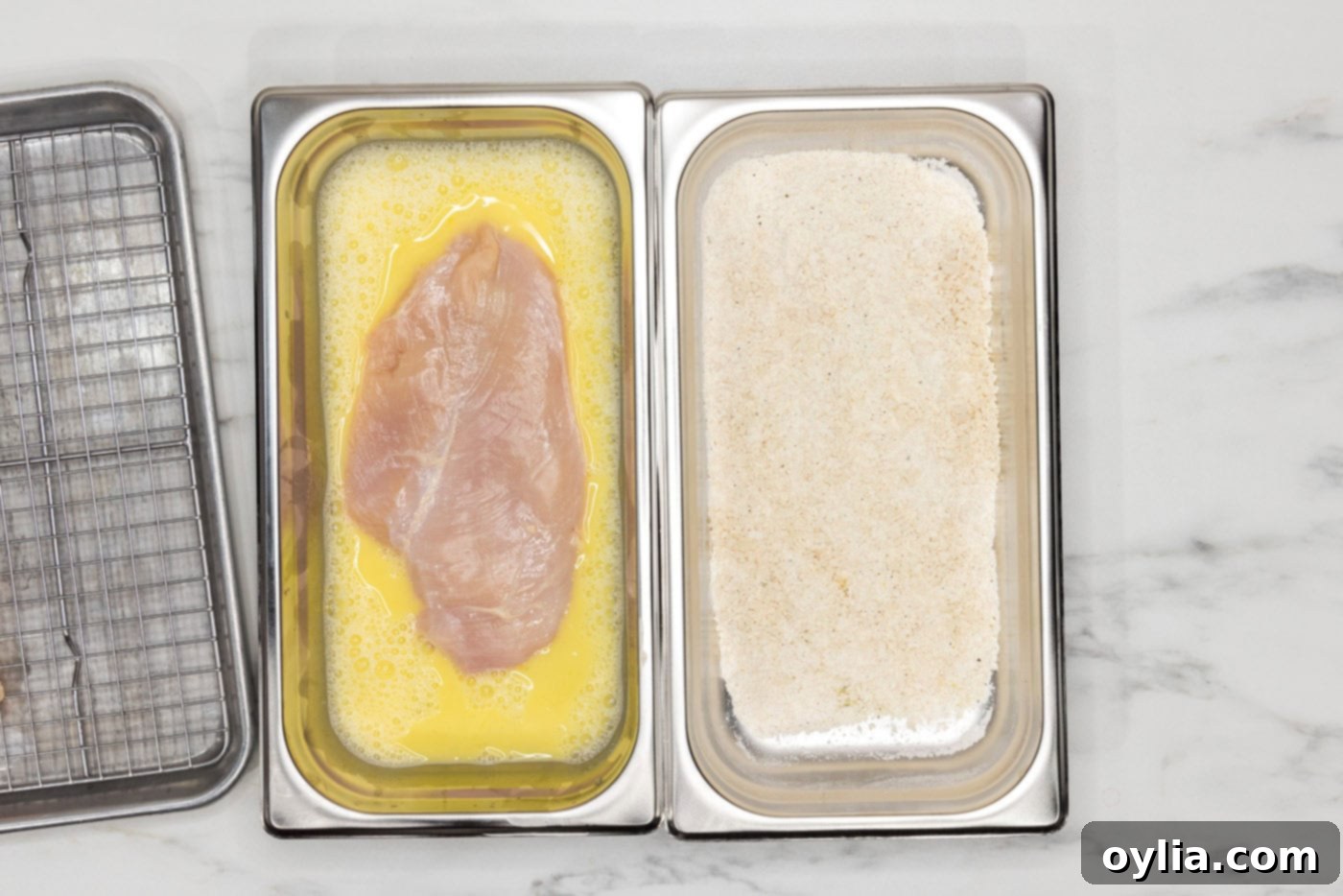 chicken breast in egg mixture inside a breading tray