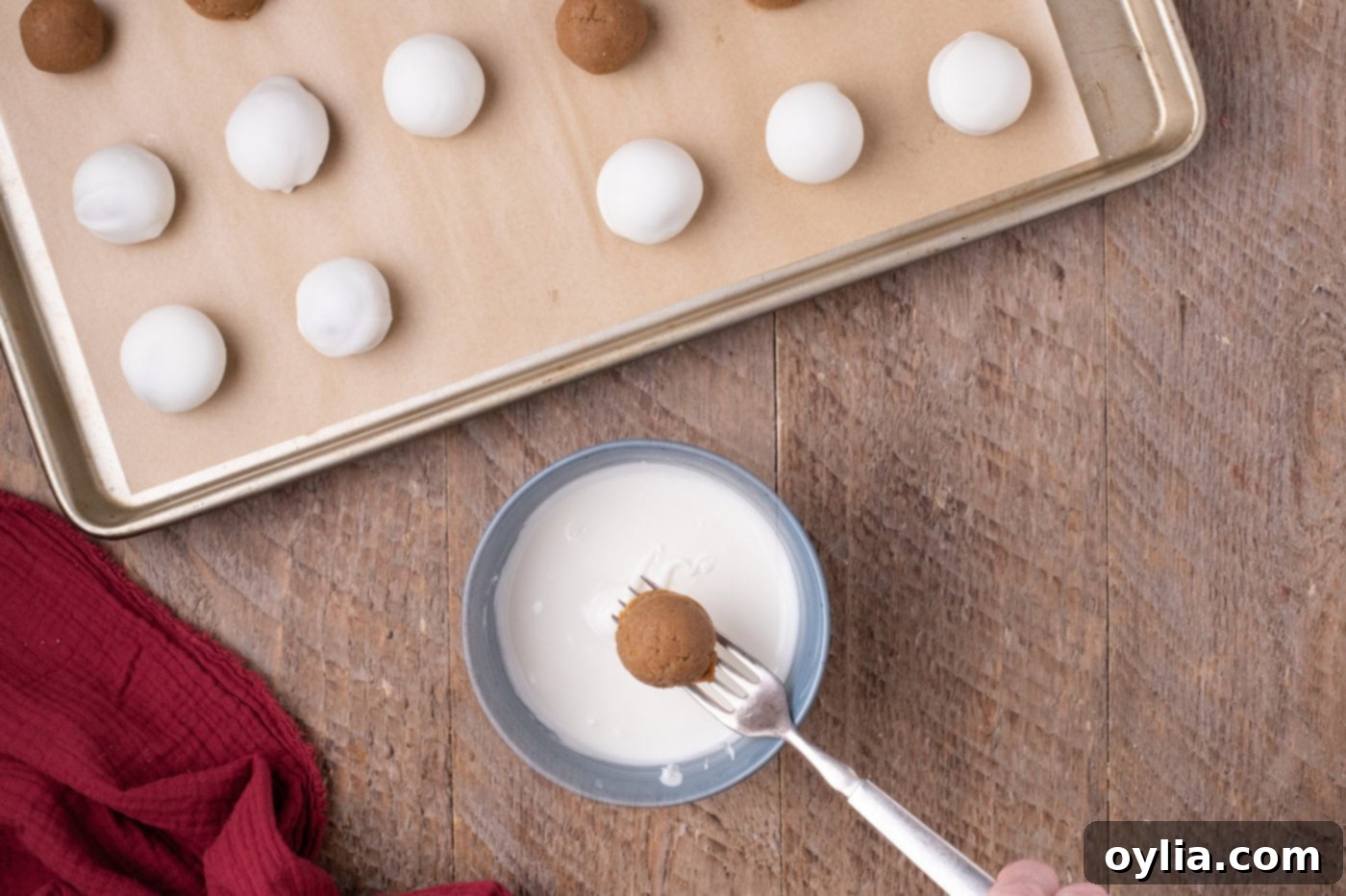 Dipping a frozen gingerbread truffle ball into melted white chocolate using a fork
