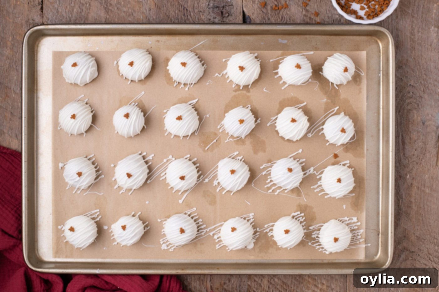 Finished gingerbread Oreo truffles on a baking sheet, drizzled with white chocolate and topped with gingerbread man sprinkles