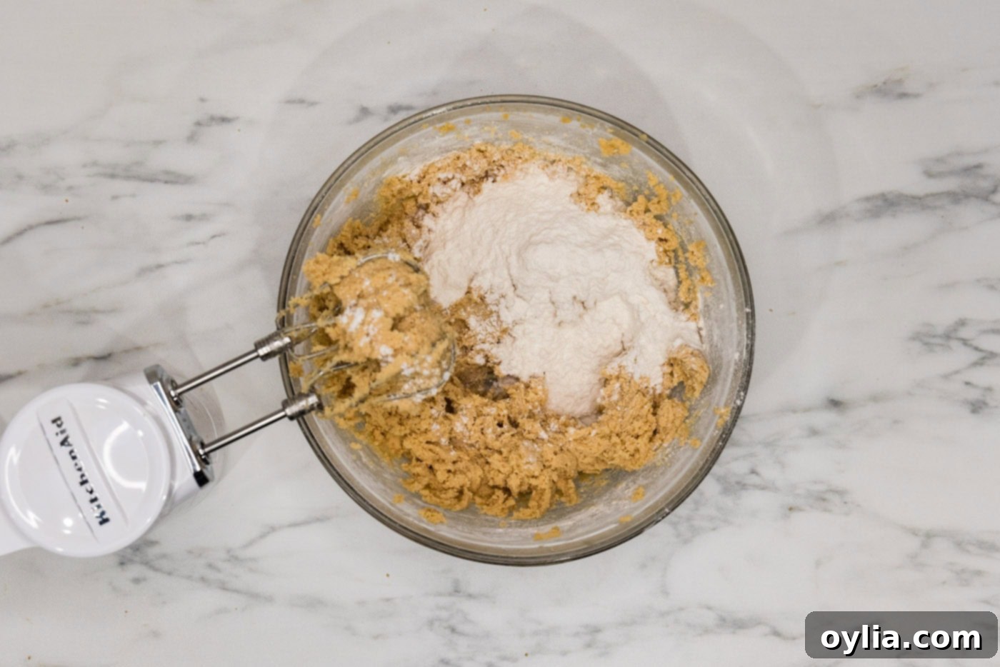 Adding dry ingredients to wet cookie dough with a hand mixer, ensuring not to overmix.
