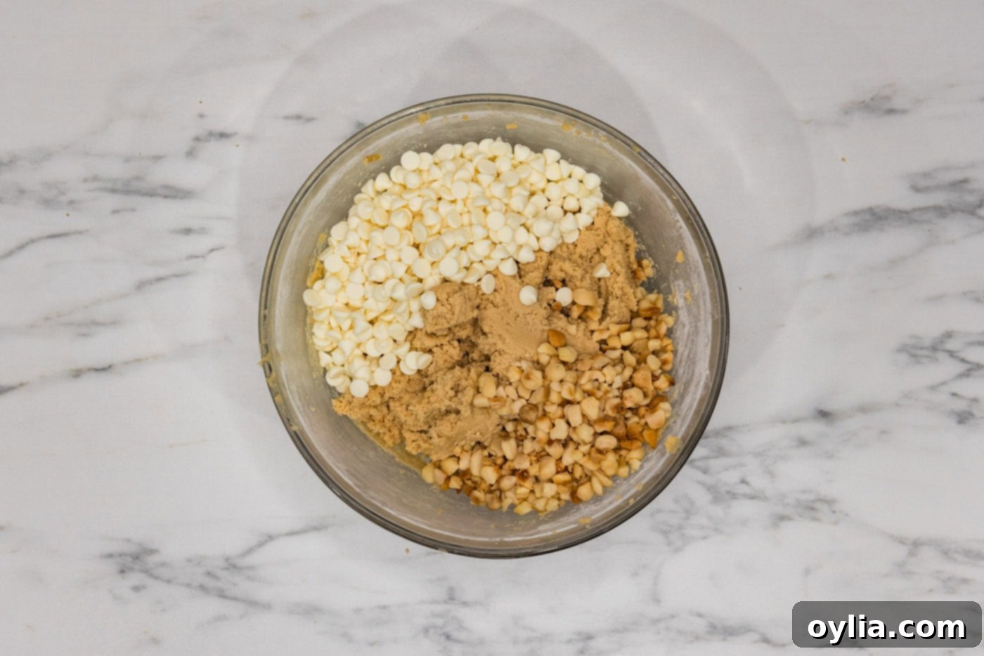 White chocolate chips and macadamia nuts added to a bowl with cookie dough, ready to be folded in.