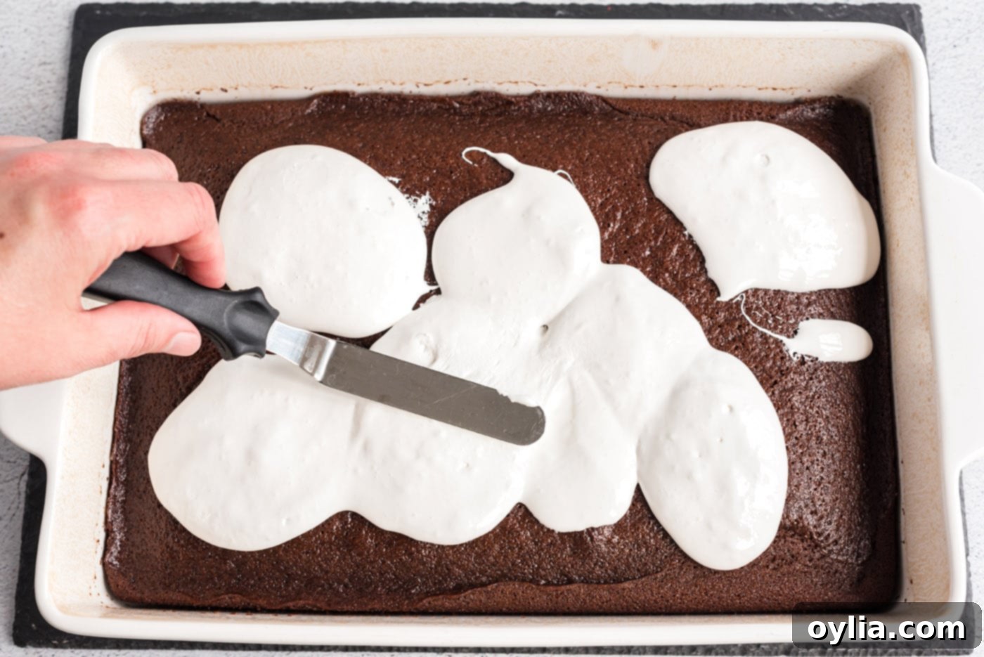 Spatula spreading marshmallow cream over the hot Coca-Cola cake