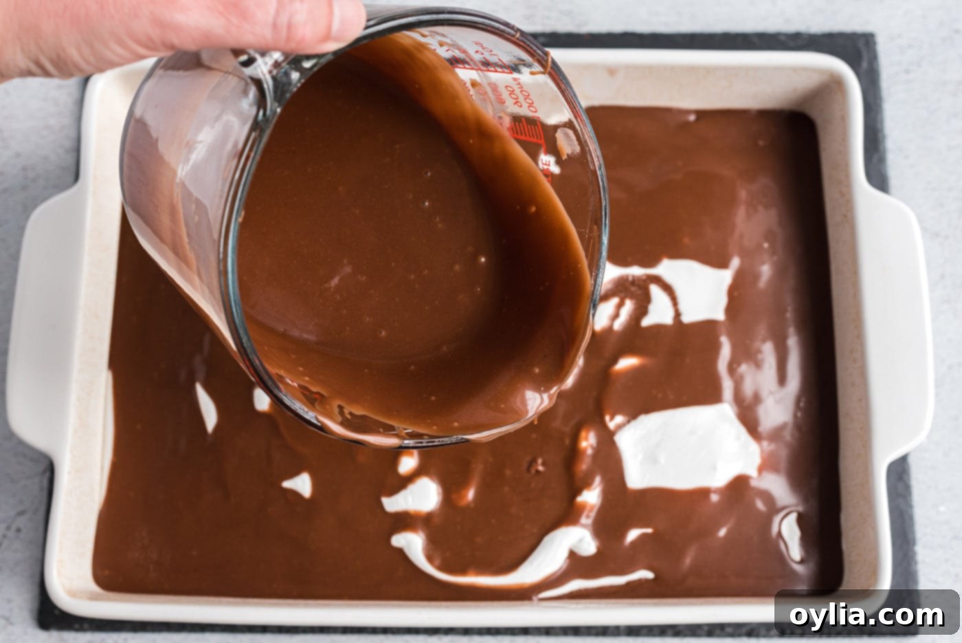 Pouring melted chocolate frosting over the marshmallow layer on the coke cake