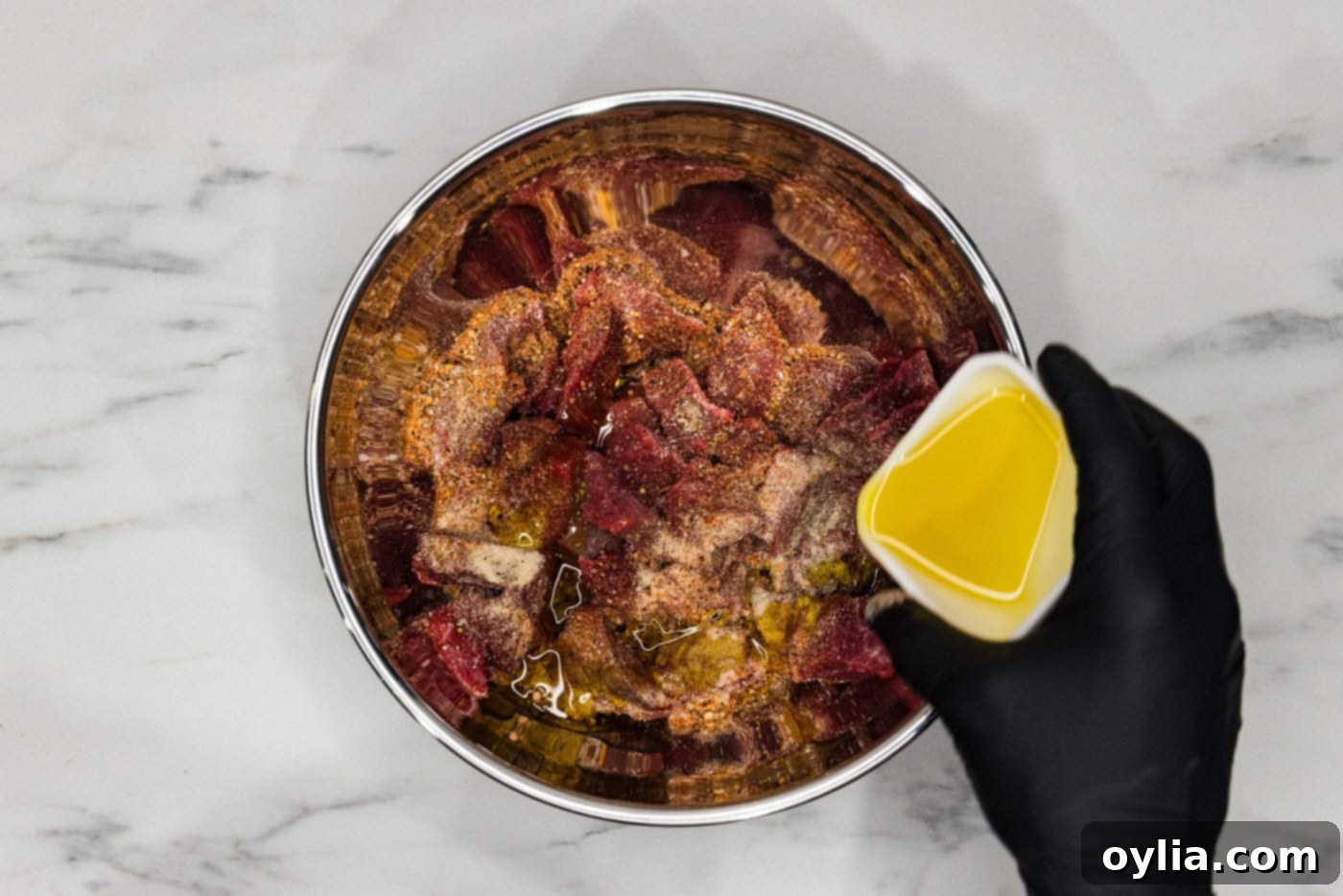 pouring olive oil into bowl of cubed steak and seasonings