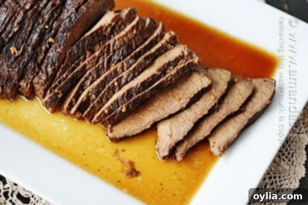 A close up overhead of sliced slow cooker roast with brandy sauce on a white platter.