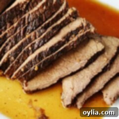 A close up of sliced slow cooker roast with brandy sauce on a white platter.