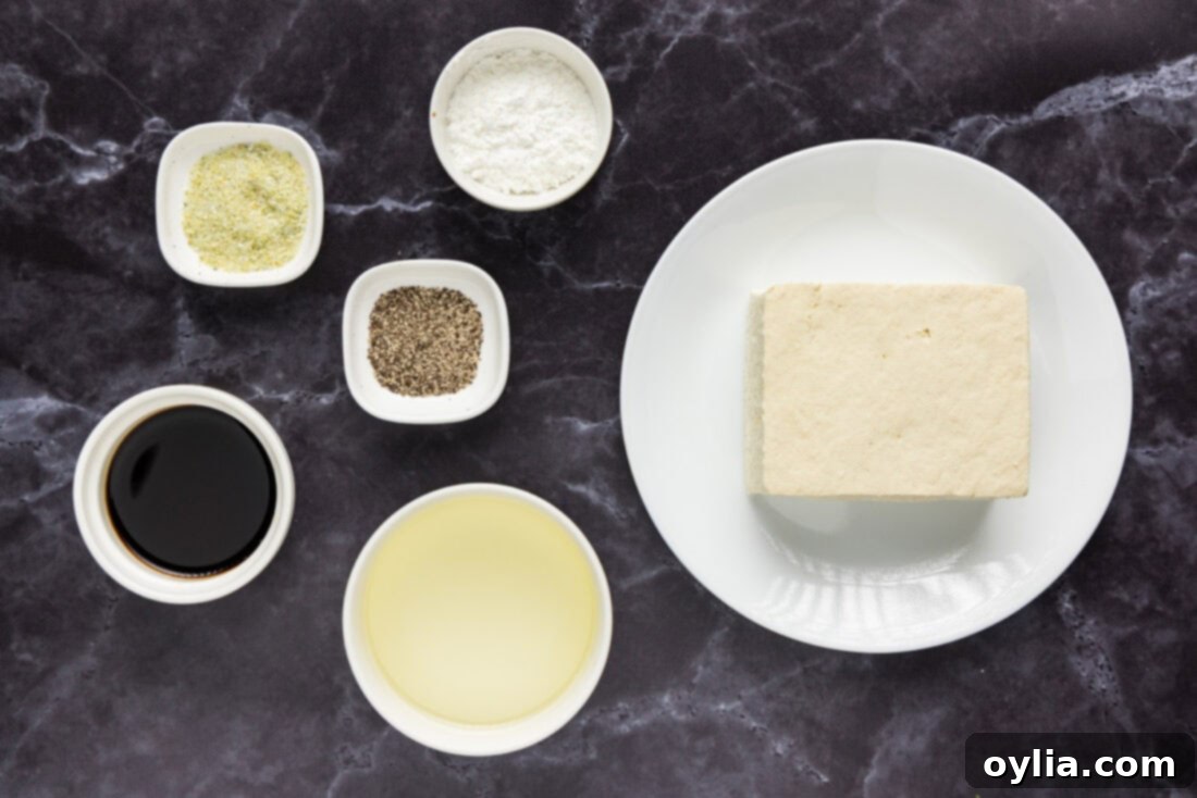 A selection of fresh ingredients including a block of tofu, a bottle of soy sauce, garlic salt, black pepper, and cornstarch, neatly arranged for making crispy fried tofu.