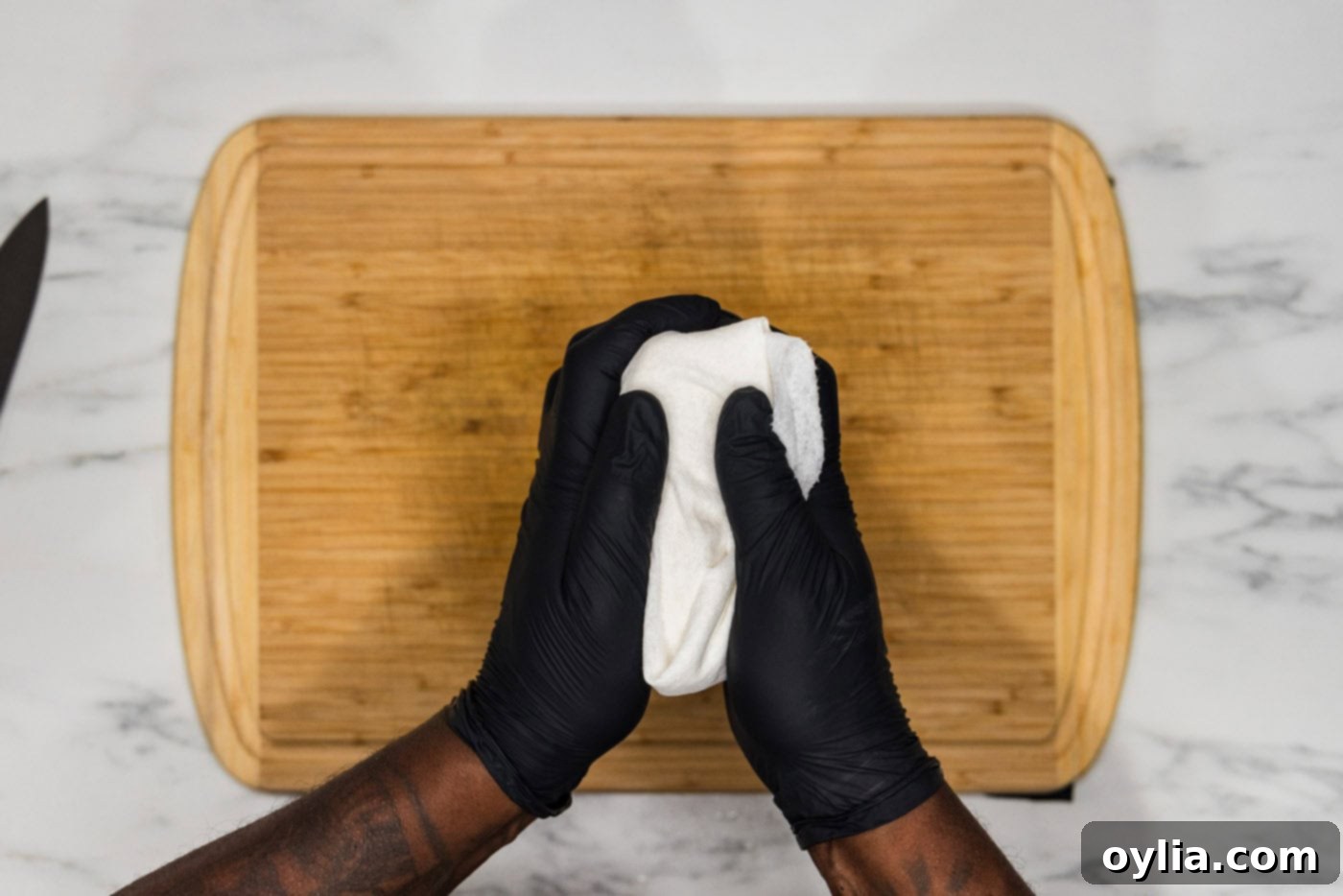 Hands pressing excess moisture from firm tofu wrapped in paper towels, a crucial step for crispy fried tofu.