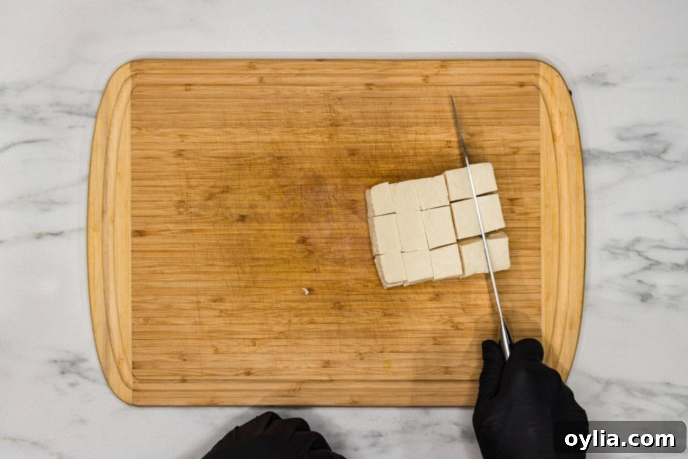Slicing a block of pressed tofu into uniform 2-inch cubes, preparing it for deep frying.