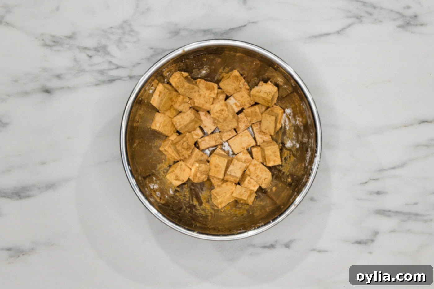 Tofu cubes coated in cornstarch and seasonings, ready for deep frying, shown in a mixing bowl.