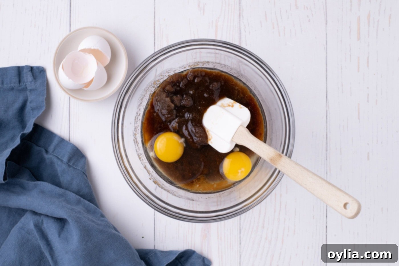 Adding eggs to a rich mixture of browned butter, dark brown sugar, and vanilla extract