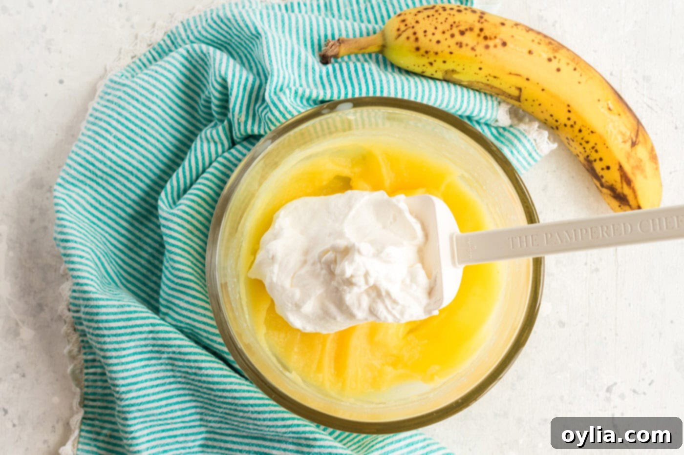 The fluffy whipped cream being gently folded into the chilled banana pudding mixture, creating a light and creamy frosting.