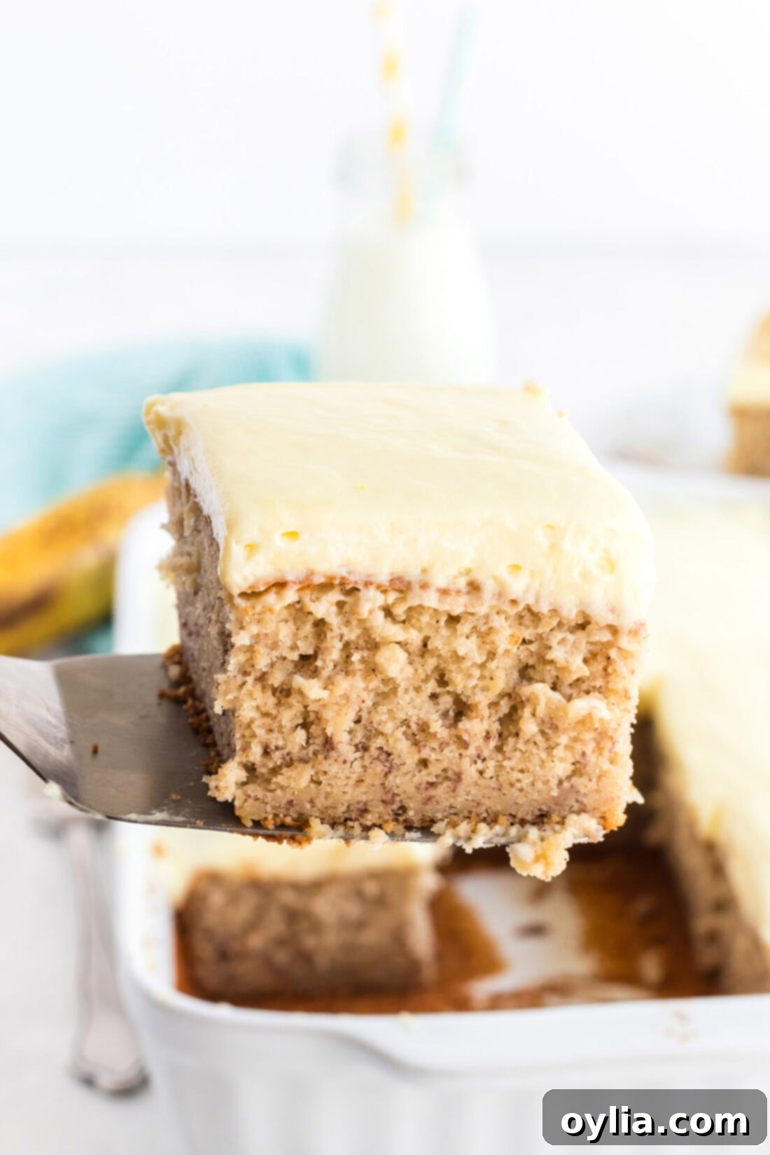 A spatula delicately lifting a slice of homemade banana cake, highlighting its rich texture and fluffy frosting.