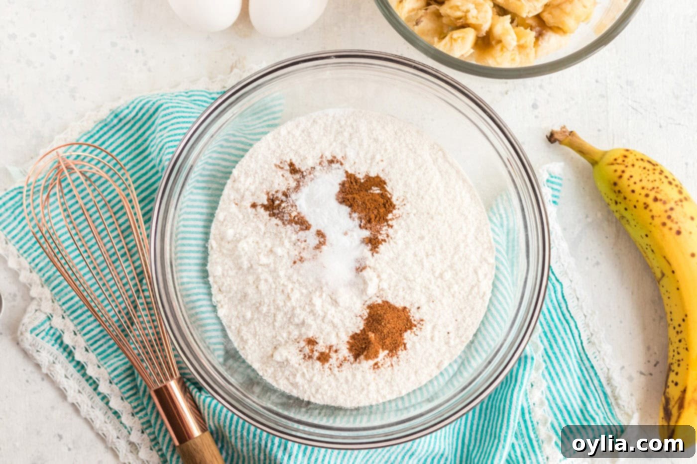 A large mixing bowl containing white cake mix with added spices like cinnamon, nutmeg, baking soda, and salt, ready to be whisked.