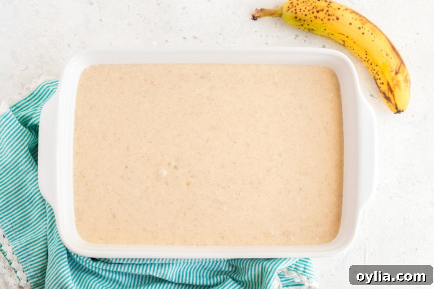 Smooth banana cake batter poured evenly into a prepared 13x9 inch baking pan, ready for the oven.