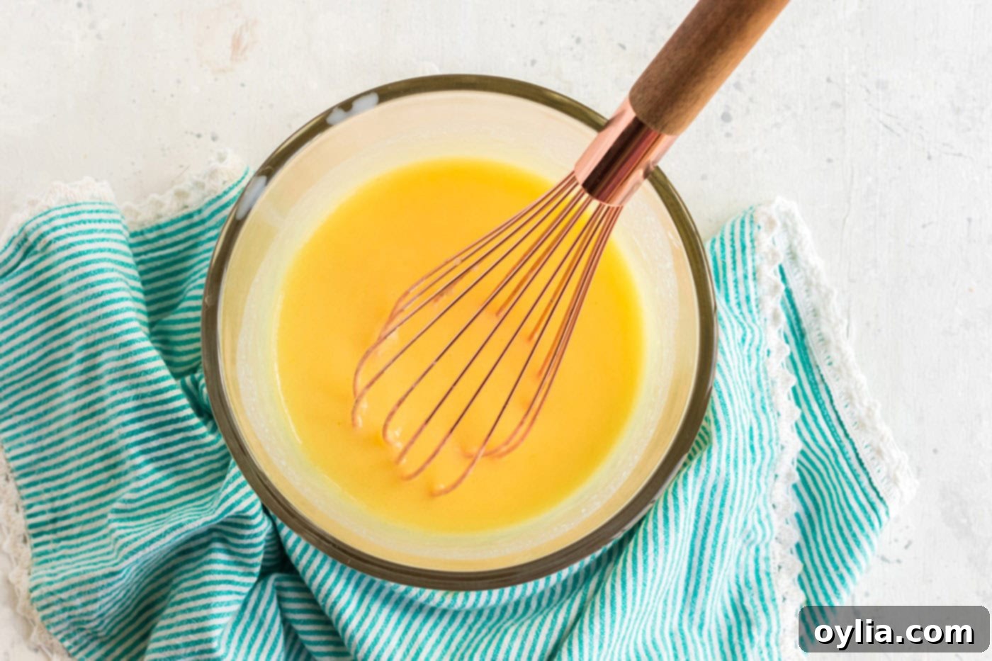 Instant banana pudding mix being whisked into milk in a medium bowl, preparing the base for the creamy frosting.