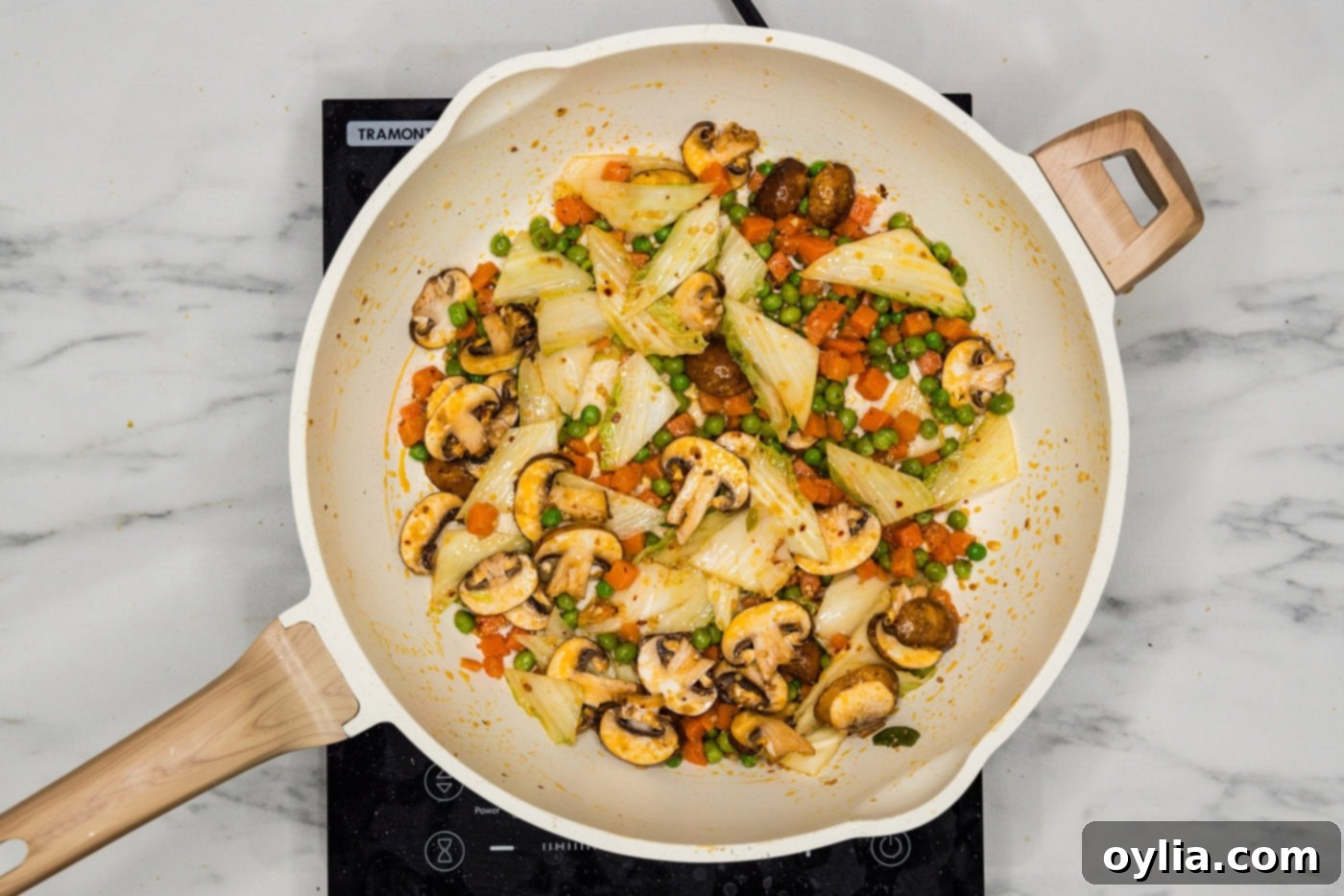 Close up of stir-fried cabbage, carrots, and peas sizzling in a skillet.