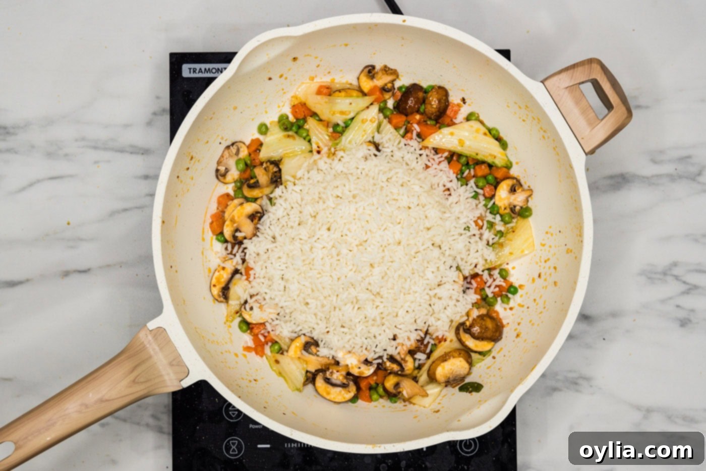 Cooked rice being added to the skillet with stir-fried vegetables.