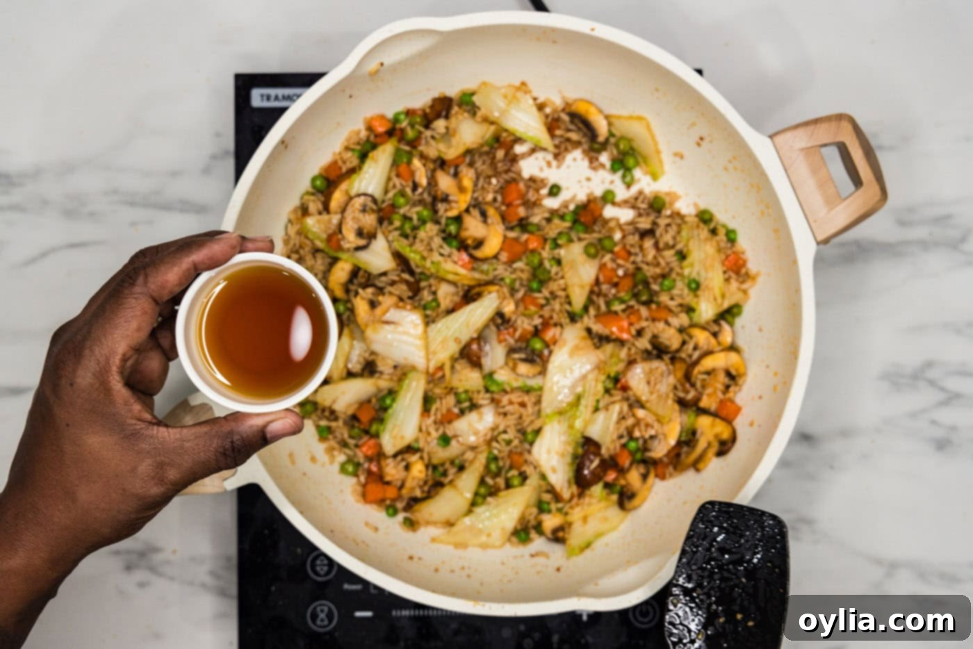Adding sesame oil to a skillet of stir-fried Korean rice and vegetables.