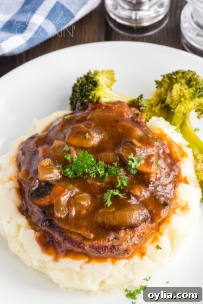 A serving of savory Swiss steak with rich gravy piled high on mashed potatoes, garnished for presentation.