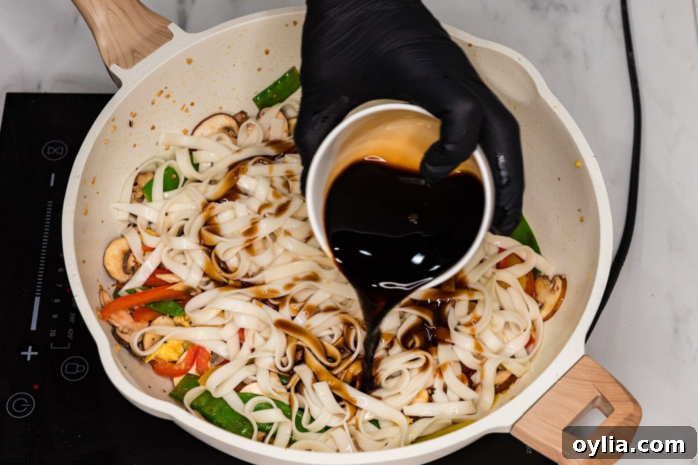 pouring sauce into skillet with vegetable lo mein