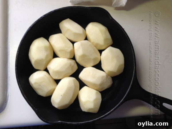 Close-up of peeled russet potatoes carefully fitted snugly into a cast iron skillet, ready for the next step.