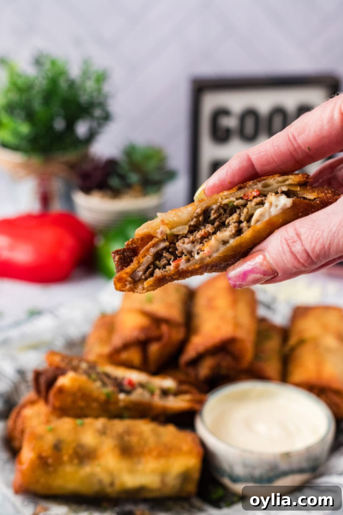 Hand holding up a Philly Cheesesteak Egg Roll cut in half revealing the gooey cheese and steak filling