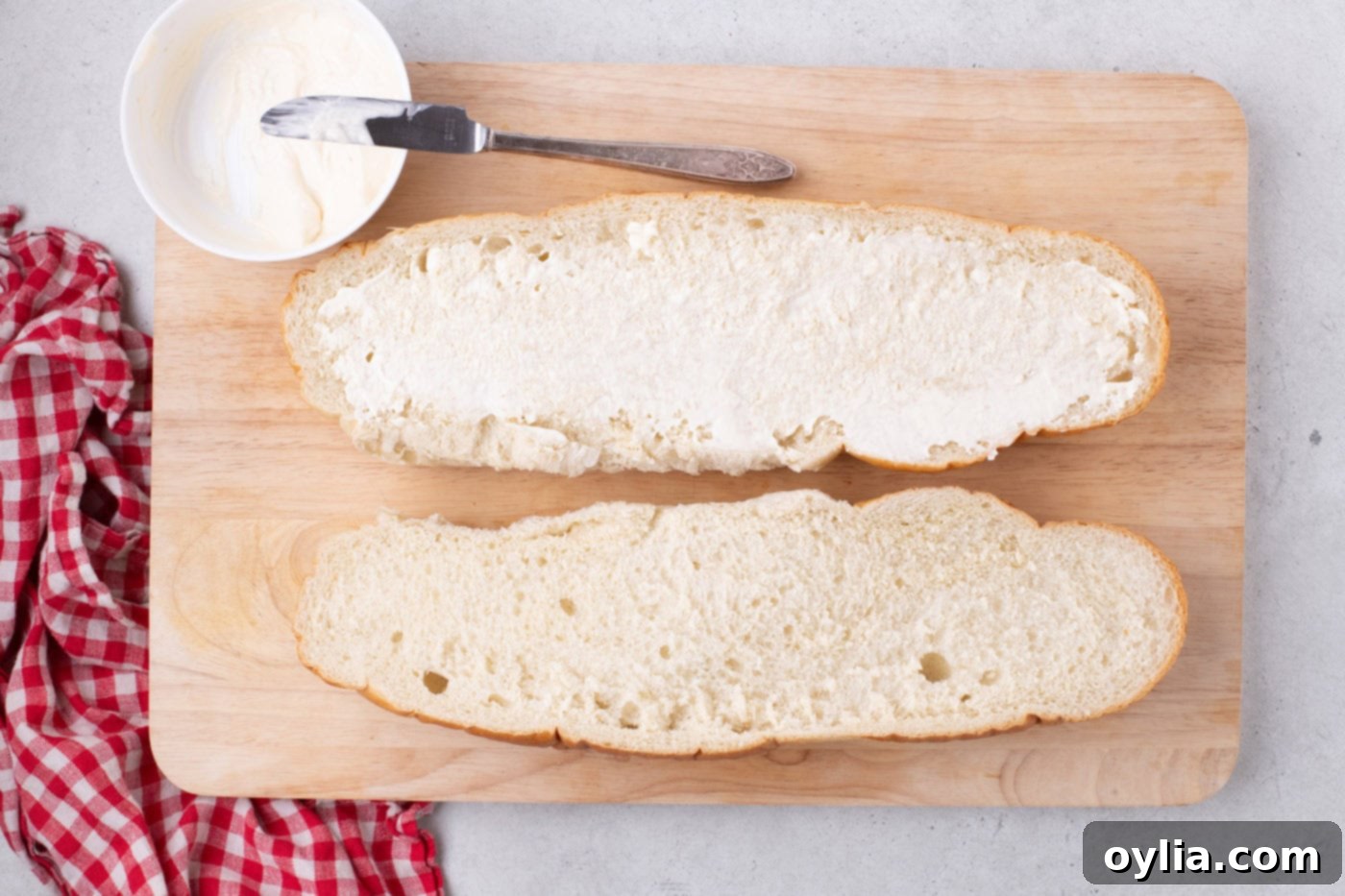 Horseradish mayo being spread evenly on a halved loaf of French bread.