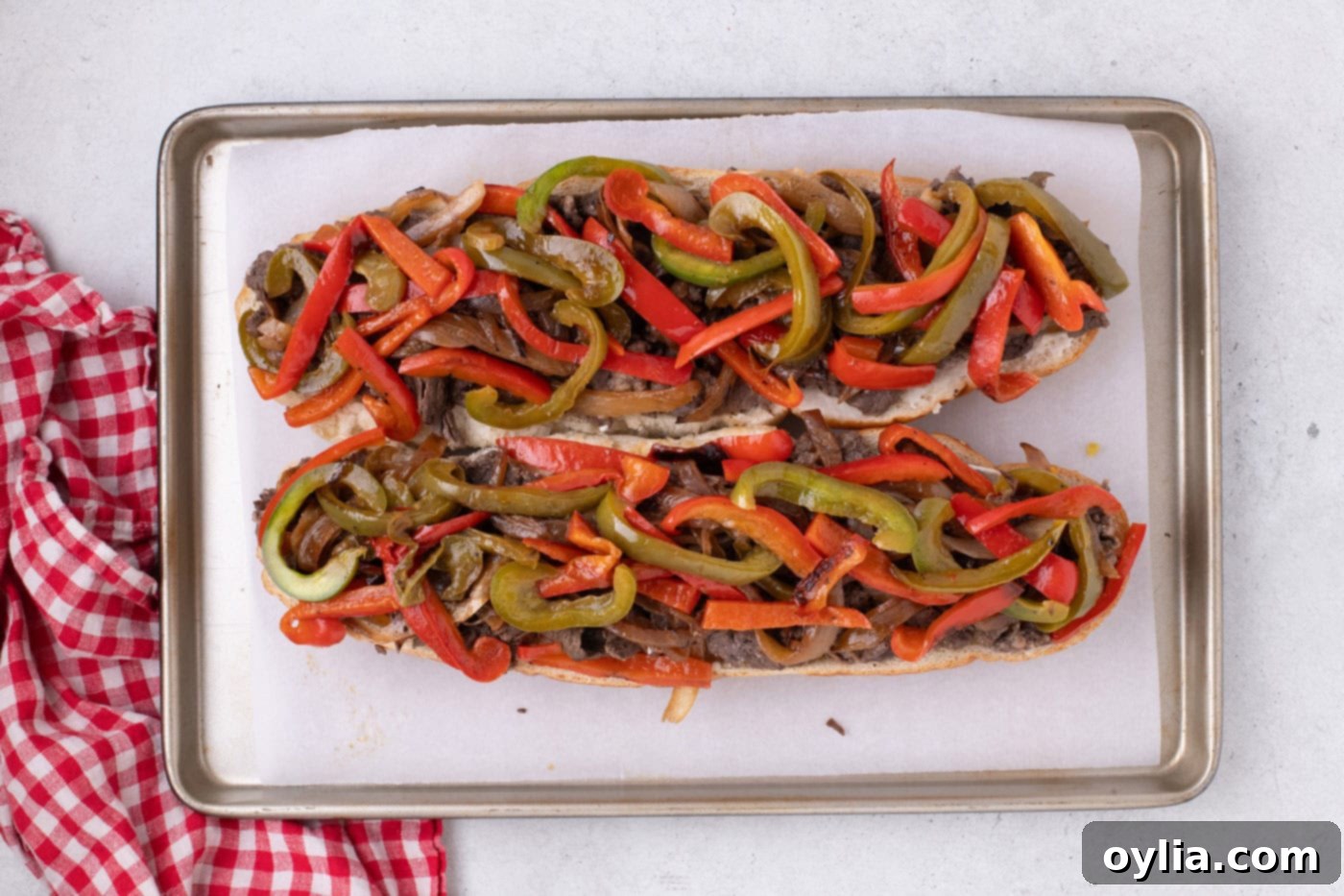 A French bread loaf generously topped with cooked steak, caramelized onions, and bell peppers.