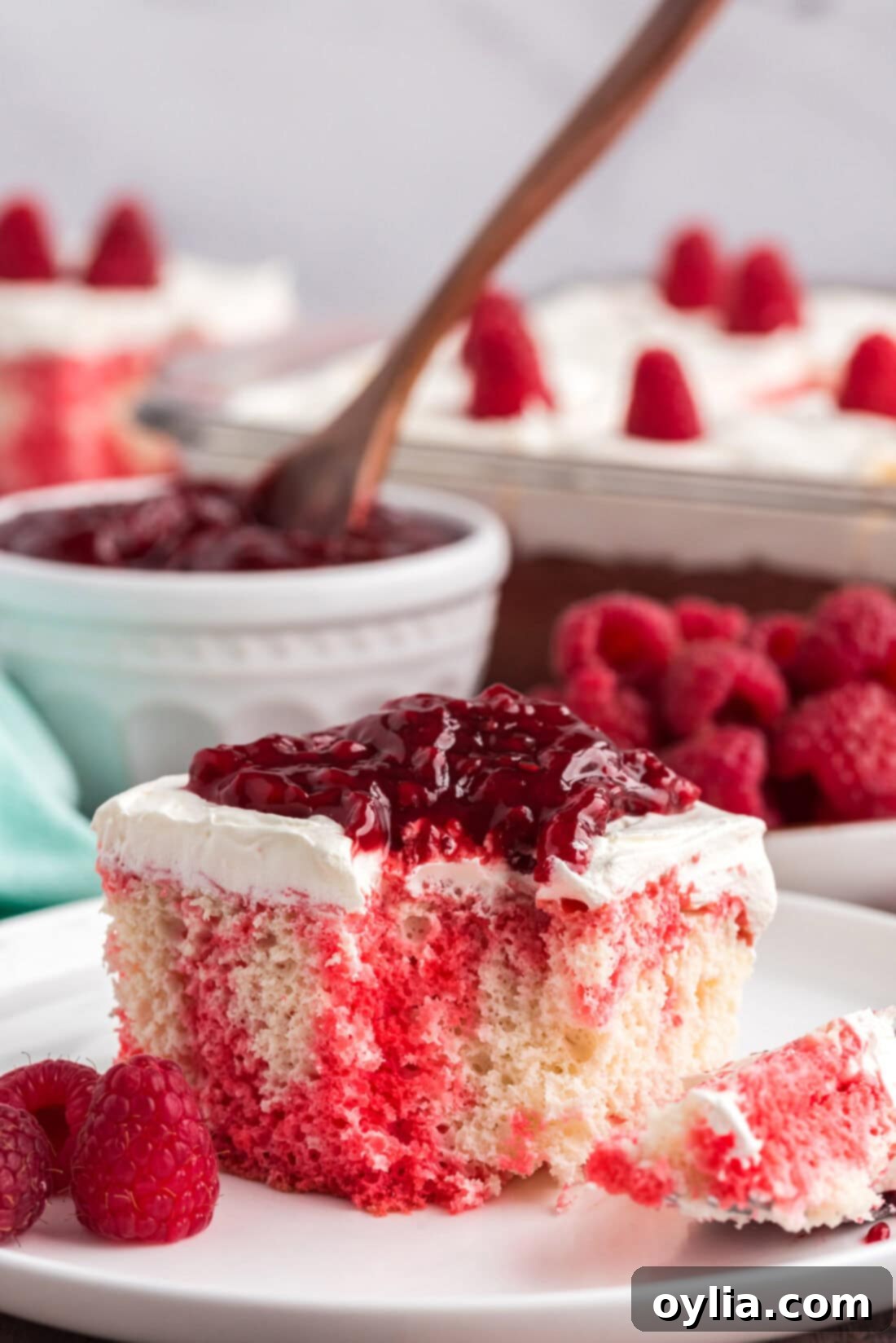 Raspberry Infusion Poke Cake 2 Slice of Raspberry Poke Cake on a plate with a bite removed, showcasing the vibrant red Jell-O seeped into the cake.