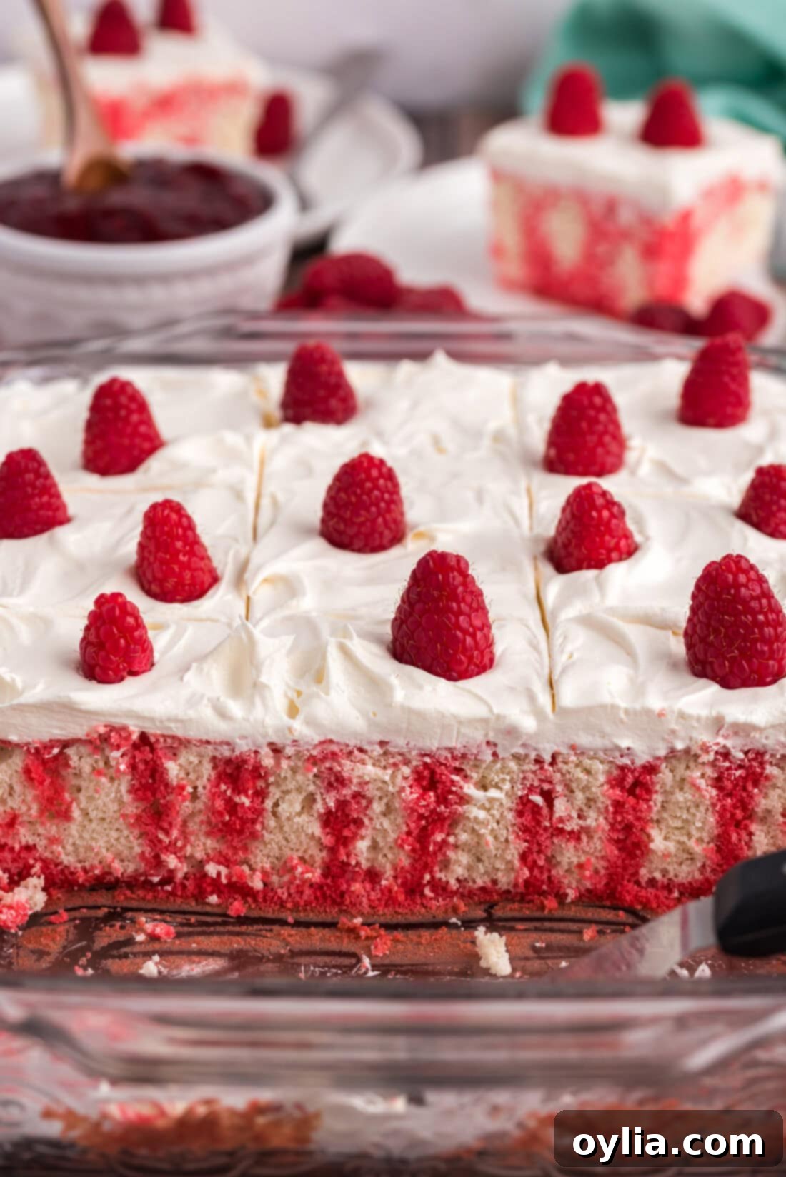 Raspberry Infusion Poke Cake 11 A pan of Raspberry Poke Cake with several slices already removed, showing the internal layers and the vibrant red Jell-O.