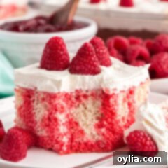 Raspberry Infusion Poke Cake 12 Close up photo of Raspberry Poke Cake on a plate with a bite removed, showing the moist cake, red Jell-O, and creamy white topping.