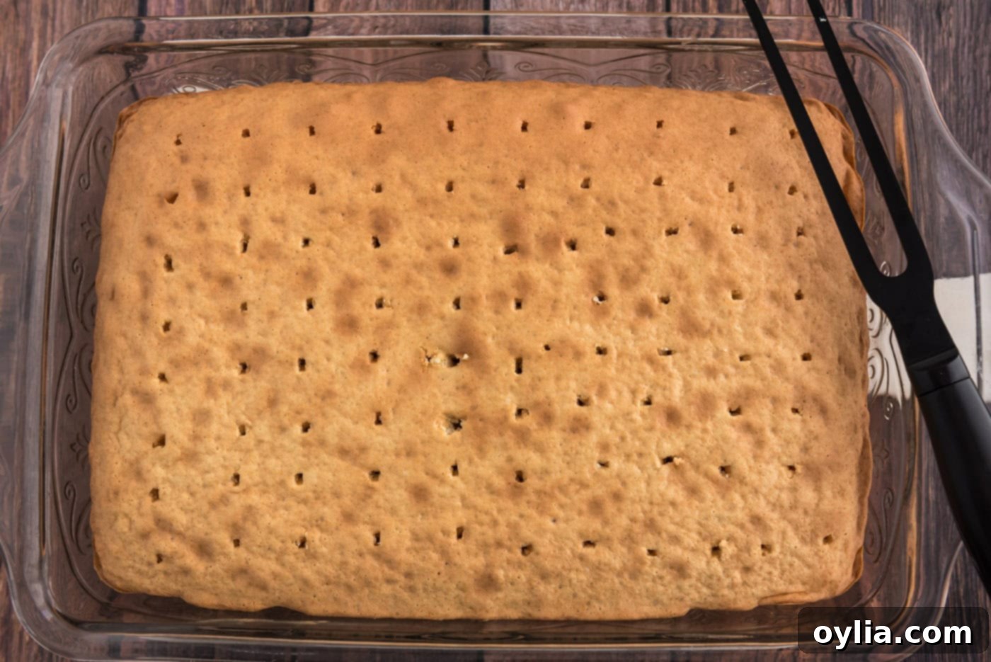 Baked cake with numerous holes poked across its surface, ready for the gelatin mixture.