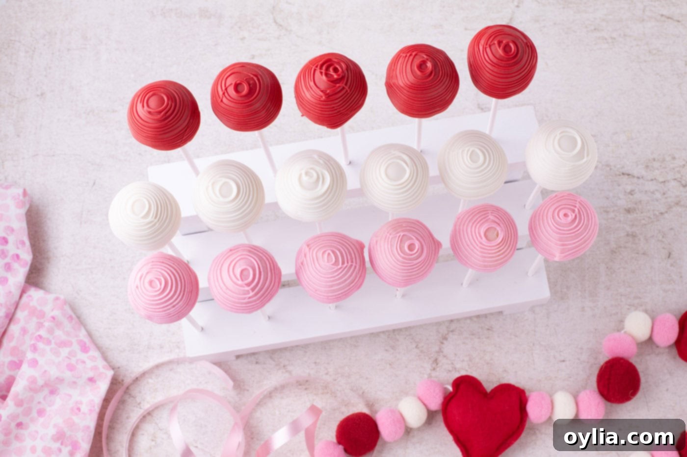 An overhead view of beautifully drizzled Valentine Cake Pops, adorned with heart sprinkles and drying on a cake pop stand.
