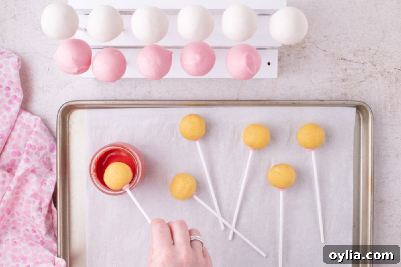 A cake pop being dipped into vibrant red melted chocolate, demonstrating the dipping technique.